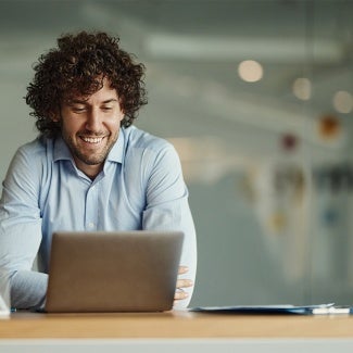 Man with curly hair and blue button up shirt working on his laptop