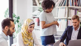 A diverse group of people collaborating around a laptop