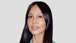 Woman with long dark hair standing in front of a light background.