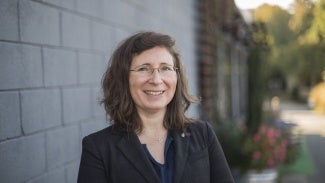 Headshot of a woman with wavy dark hair wearing a dark jacket and glasses