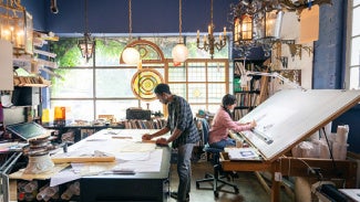 Two people stand back to back, each working at their own large surface in the work area/office