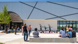Exterior of Collage Dance building, three dancers perform outdoors in front of small audience.