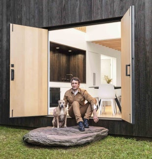 A man and dog sit in double exterior doors on the Bovina Cabin in Hudson Valley, New York.