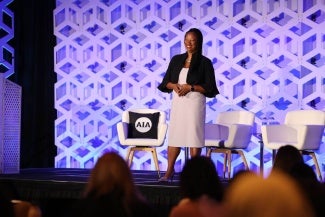 Lakisha Woods, AIA EVP/CEO, stands onstage in front of a purple geometric background at the 2024 Women's Leadership Summit in Chicago