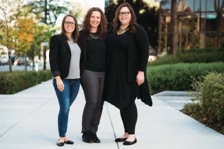 This is an image of three women architects standing and posing together for a picture on a sidewalk outside