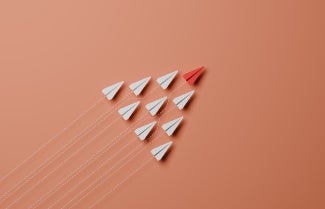 photo illustration red paper airplane leading formation of white paper airplanes