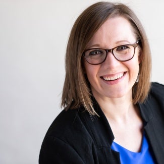 Headshot of a woman with short brown hair wearing glasses and a dark jacket 