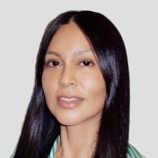 Woman with long dark hair standing in front of a light background.