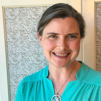 A woman in a teal top stands in front of a decorative shade.