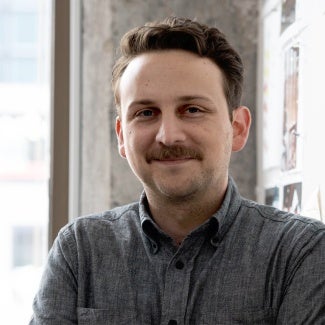 Headshot of a man with dark hair and a mustache wearing a gray shirt. 