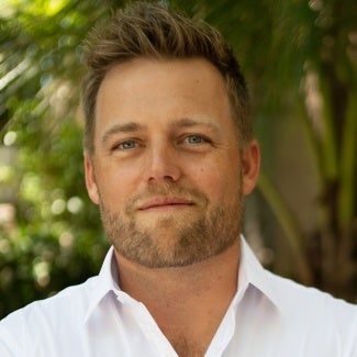 Head shot of a man with short blonde hair wearing a light shirt