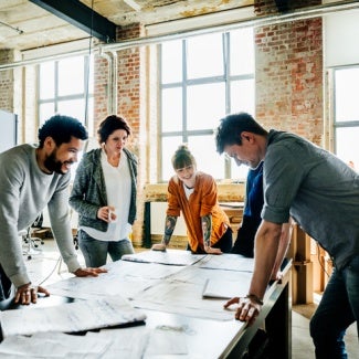 Group of architects standing around table with blueprints