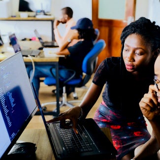 two coworkers leaning over a computer screen collaborating